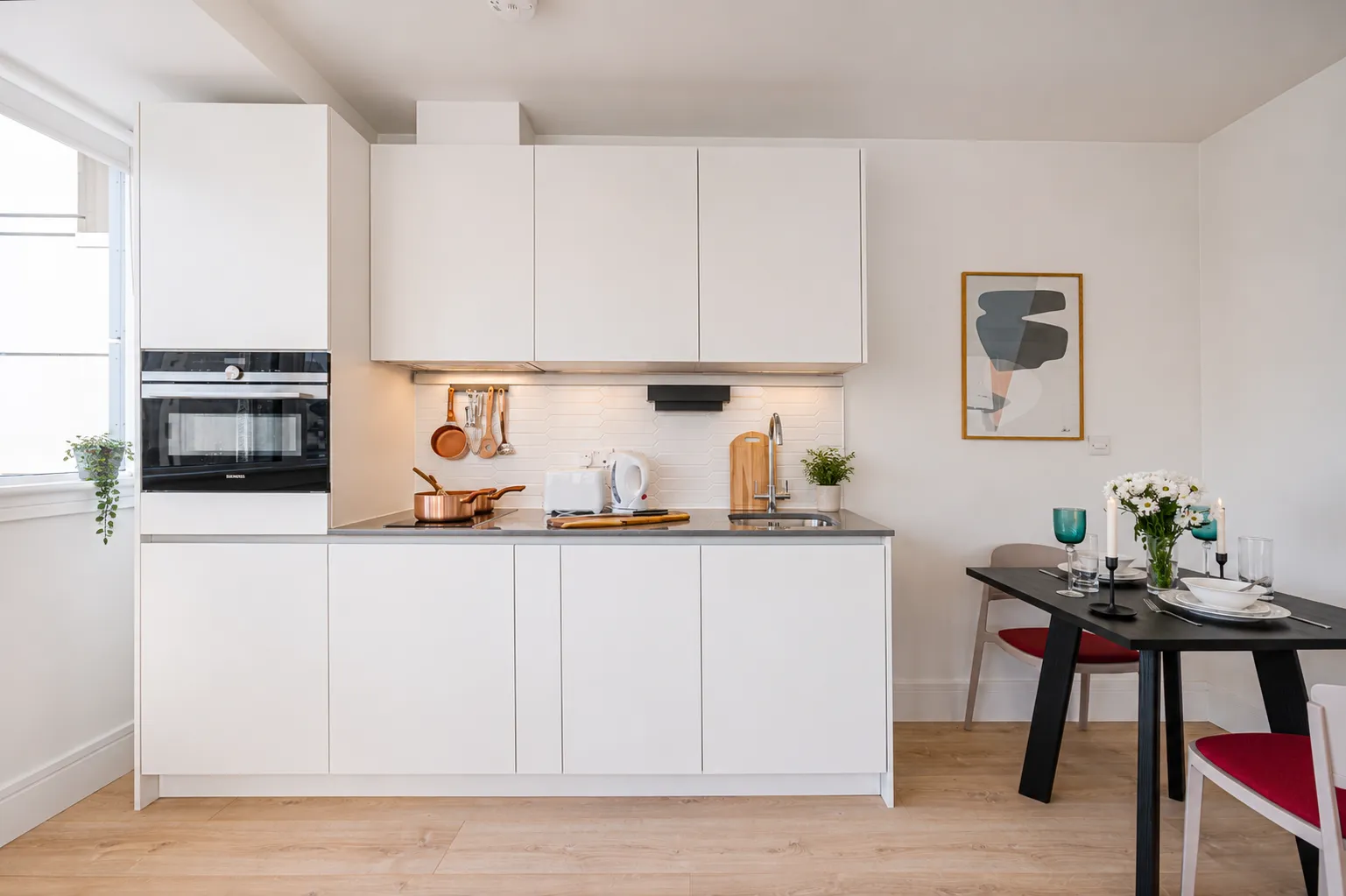 White fitted kitchen with an integrated oven and a dining table, in a one-bedroom flat at Vonder Wembley