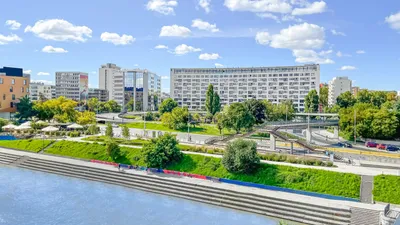 Vonder Upriver seen across the river, with landscaped riverside gardens in front of the buildings