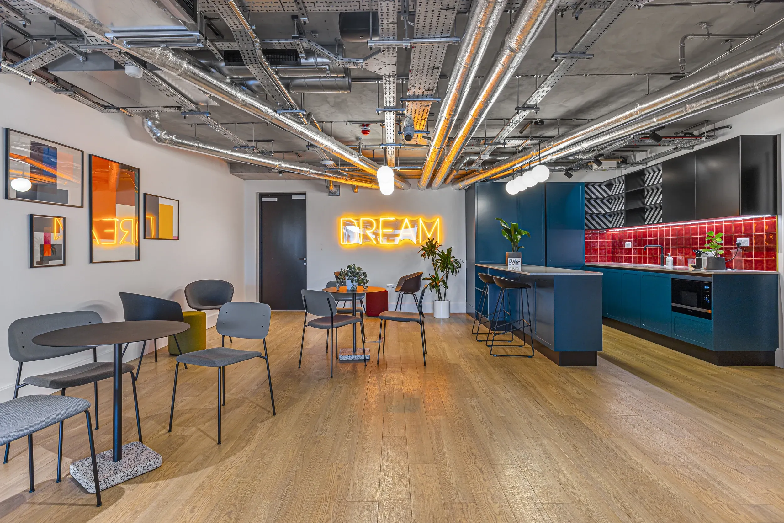 Communal kitchen and cafe area at Vonder Wembley, with bar seating, blue kitchen units and a neon sign